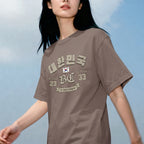 Lifestyle shot of a woman wearing a brown K-citizen t-shirt with a vintage collegiate Korean Hangul "대한민국" (Daehanminguk) typo
