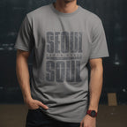 Model wearing a gray t-shirt with a distressed dark gray "SEOUL SOUL" graphic and South Korea coordinates against a dark studio background