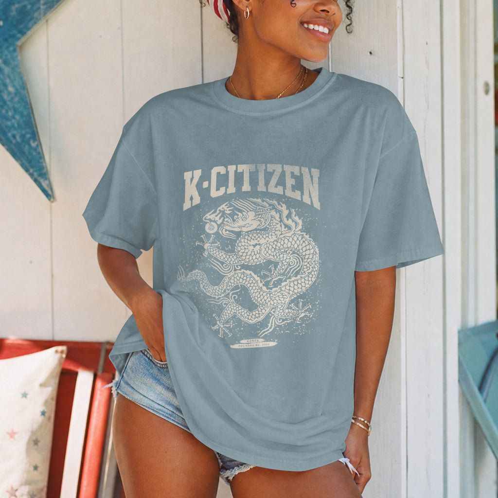 Person wearing a blue t-shirt with 'K-Citizen' and korean royal dragon design in summer cottage background