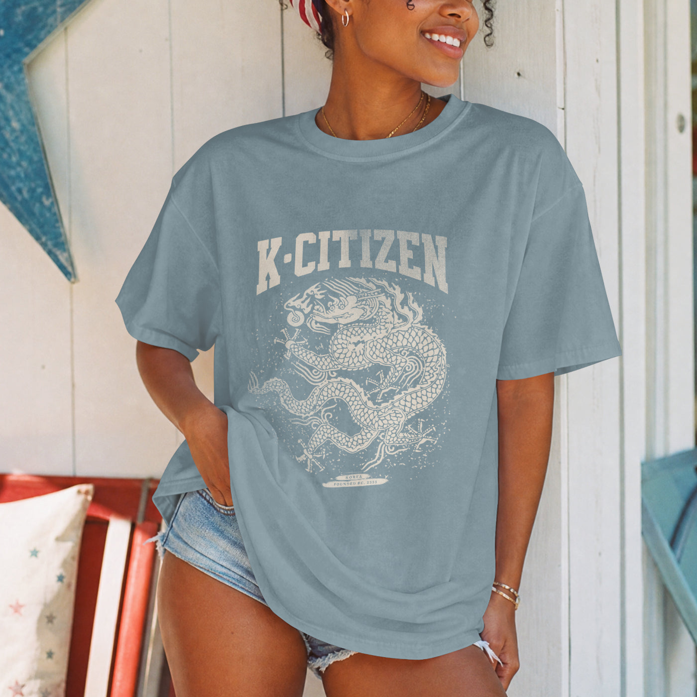 Person wearing a blue t-shirt with 'K-Citizen' and korean royal dragon design in summer cottage background