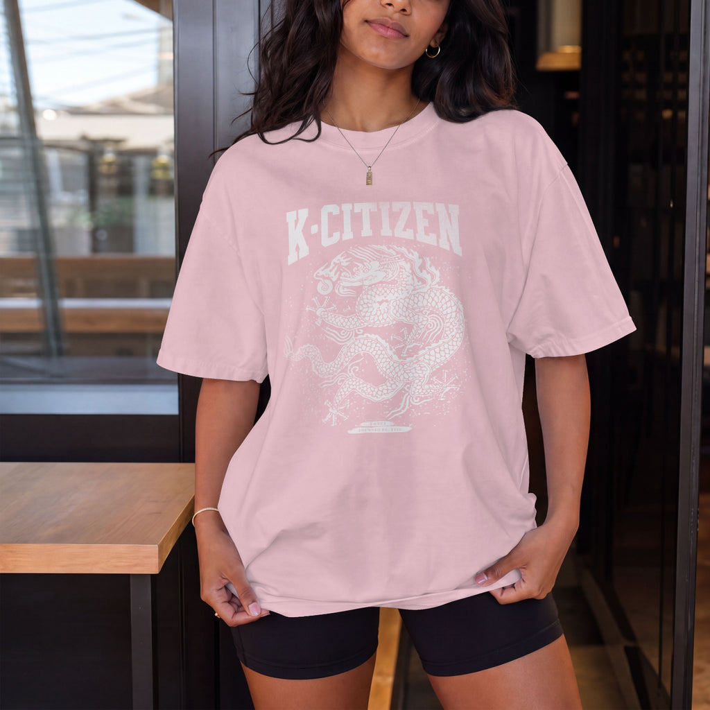 Person wearing a pink 'K-Citizen' t-shirt with a dragon design indoors.