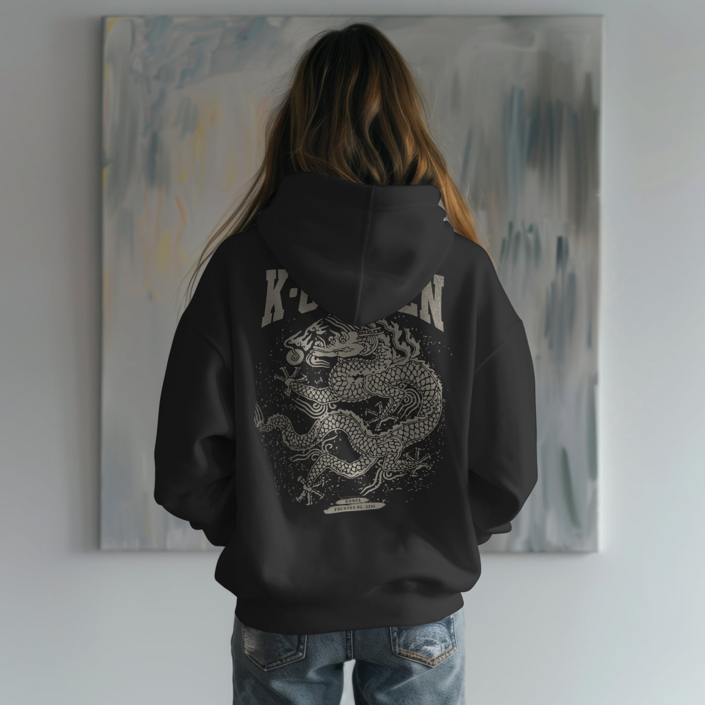 Person wearing a black hoodie with a dragon design in front of a painting