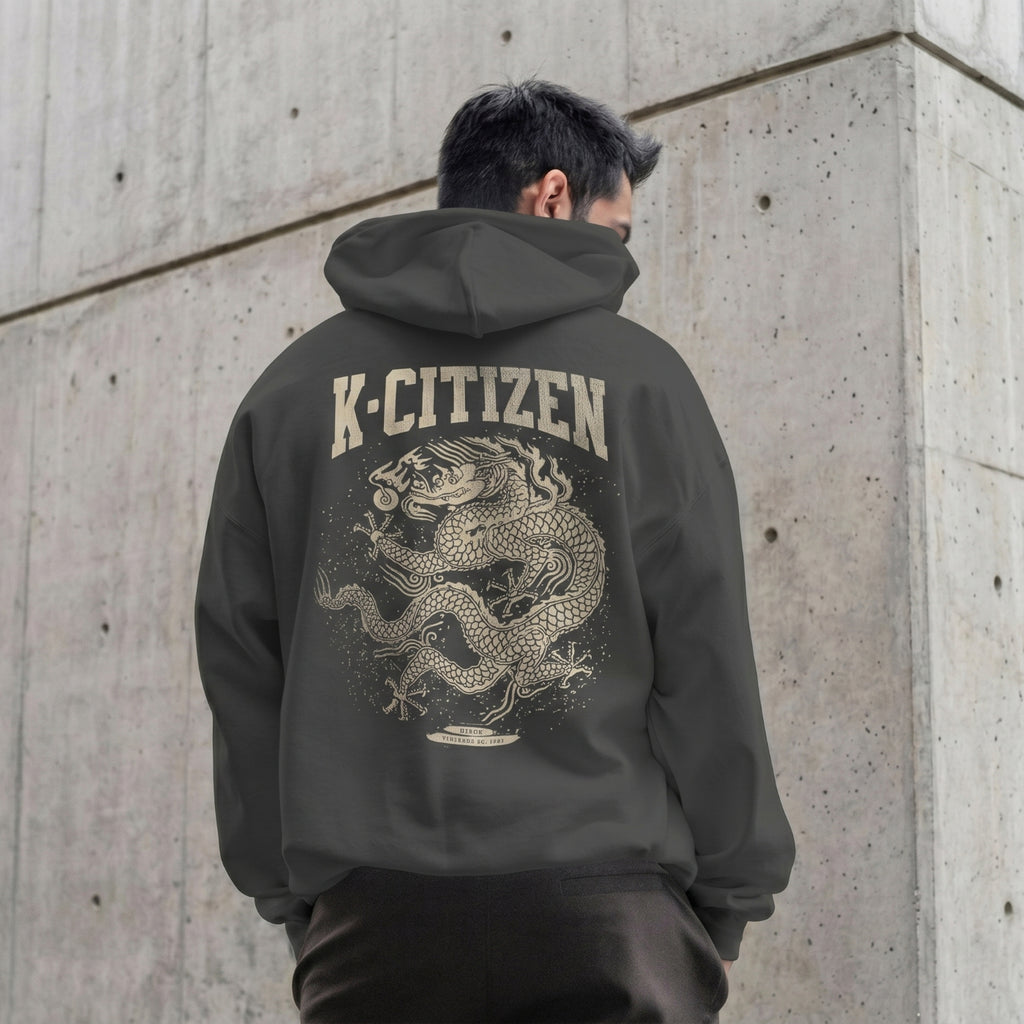 Person wearing a hoodie with a dragon design and 'K-Citizen' text on the back, standing against a concrete wall.