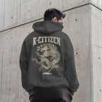 Person wearing a hoodie with a dragon design and 'K-Citizen' text on the back, standing against a concrete wall.
