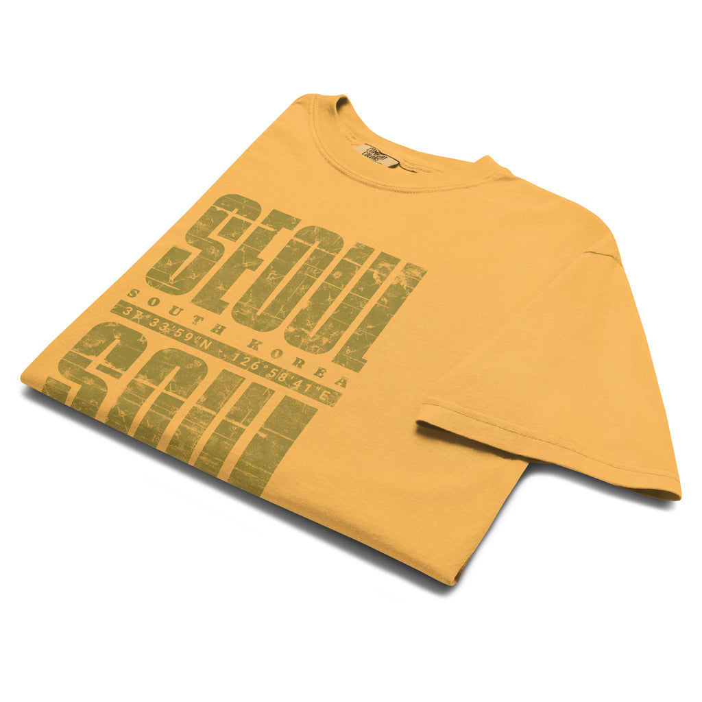 Close-up mustard color t-shirt featuring a distressed white "SEOUL SOUL" graphic with South Korea geographic coordinates